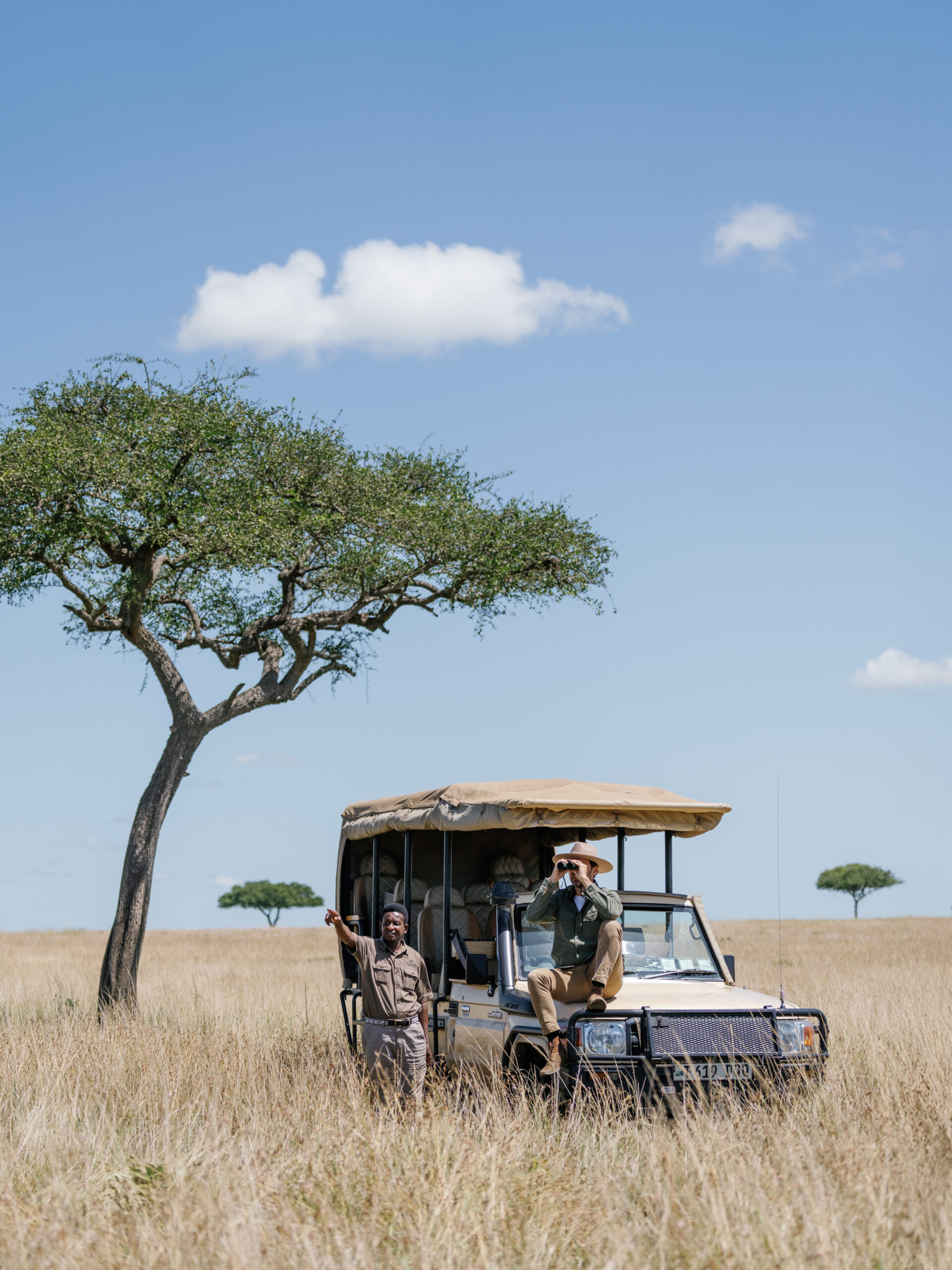 Guests on a guided game drive in an open-air safari vehicle, observing wildlife across the African savanna with an expert guide